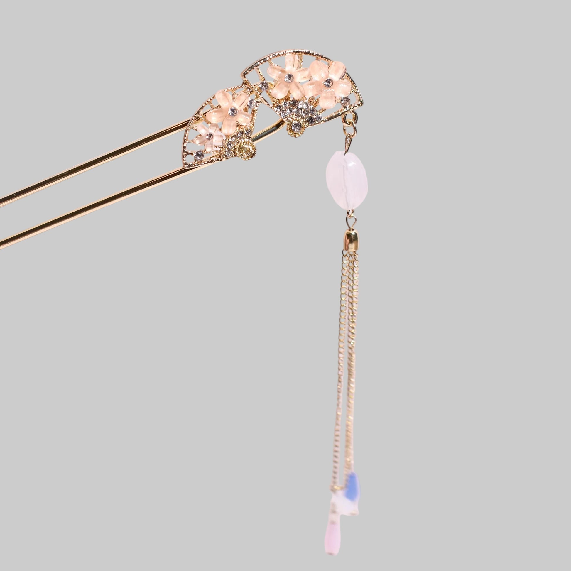 Decorative hairpin with gemstones and a tassel on a pink background